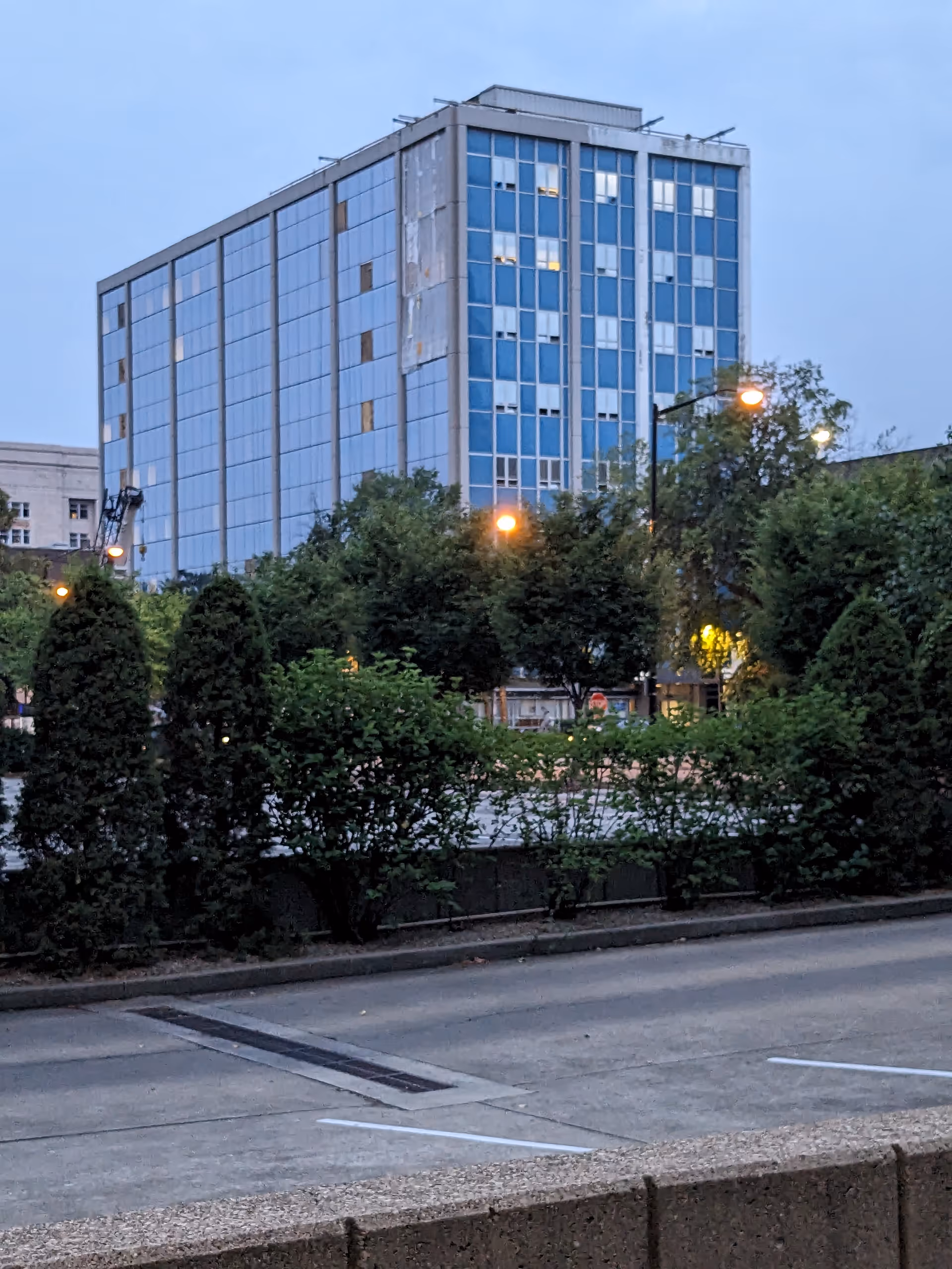 Exterior view of a tall blue-glass building in downtown, with trees and street in foreground.