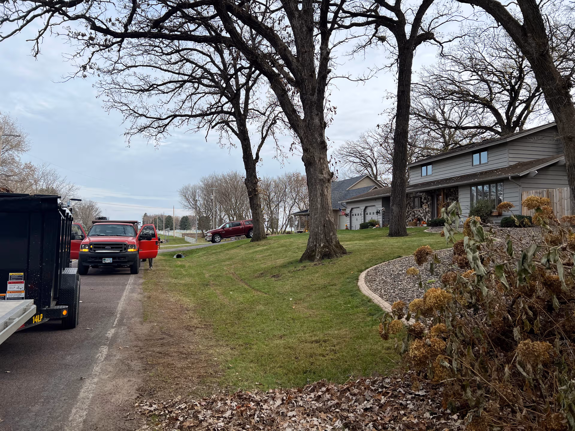 Exterior view of Traditions of Owatonna with lawn, trees, and parked vehicles.