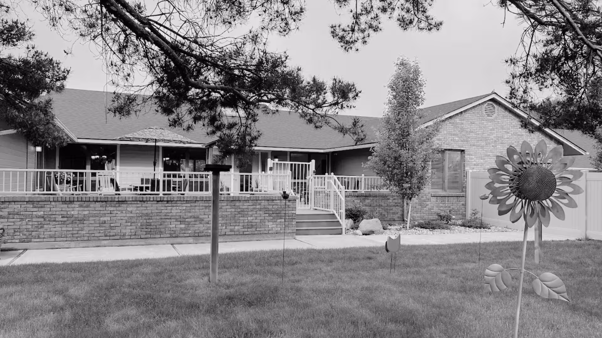 Single-story brick senior living facility with front porch and a large sunflower sculpture in yard.