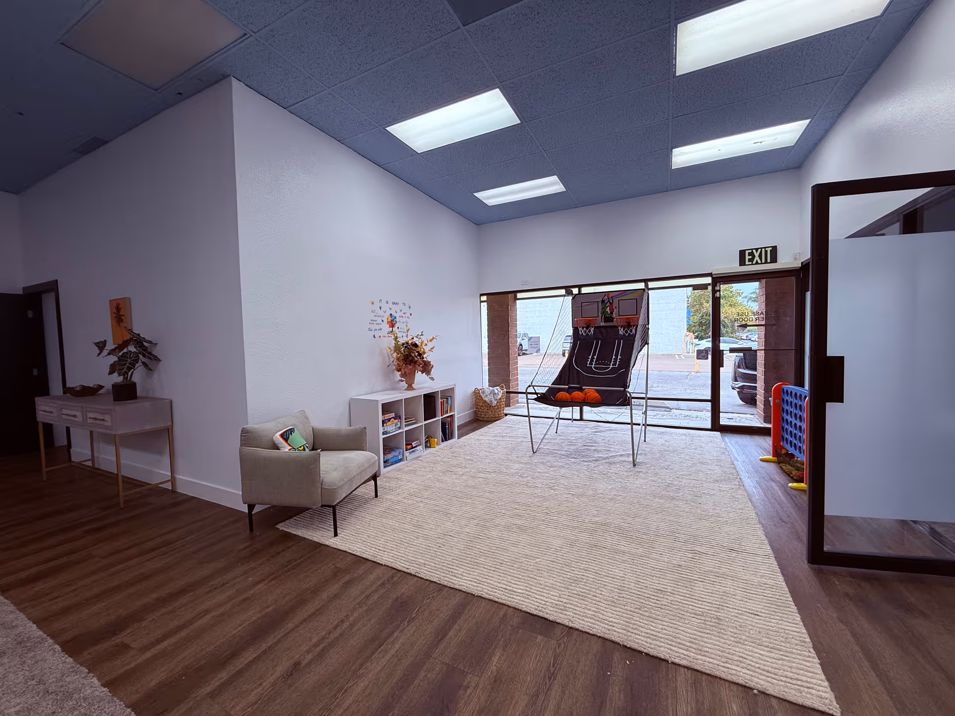 Interior lobby of a senior facility with seating, rug, shelves, and glass exit doors.