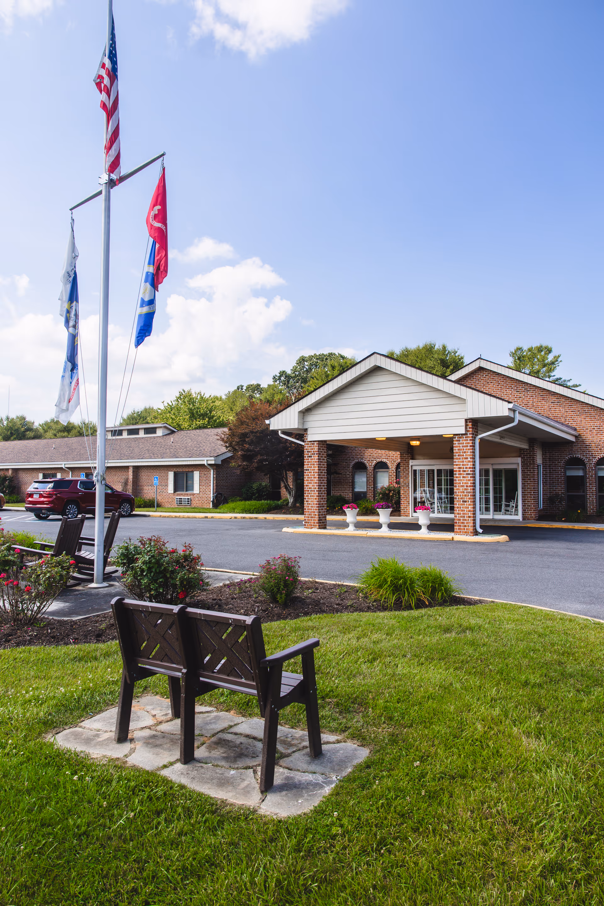 Exterior view of Commonwealth Senior Living at Hillsville with flagpoles, entrance canopy, and bench.