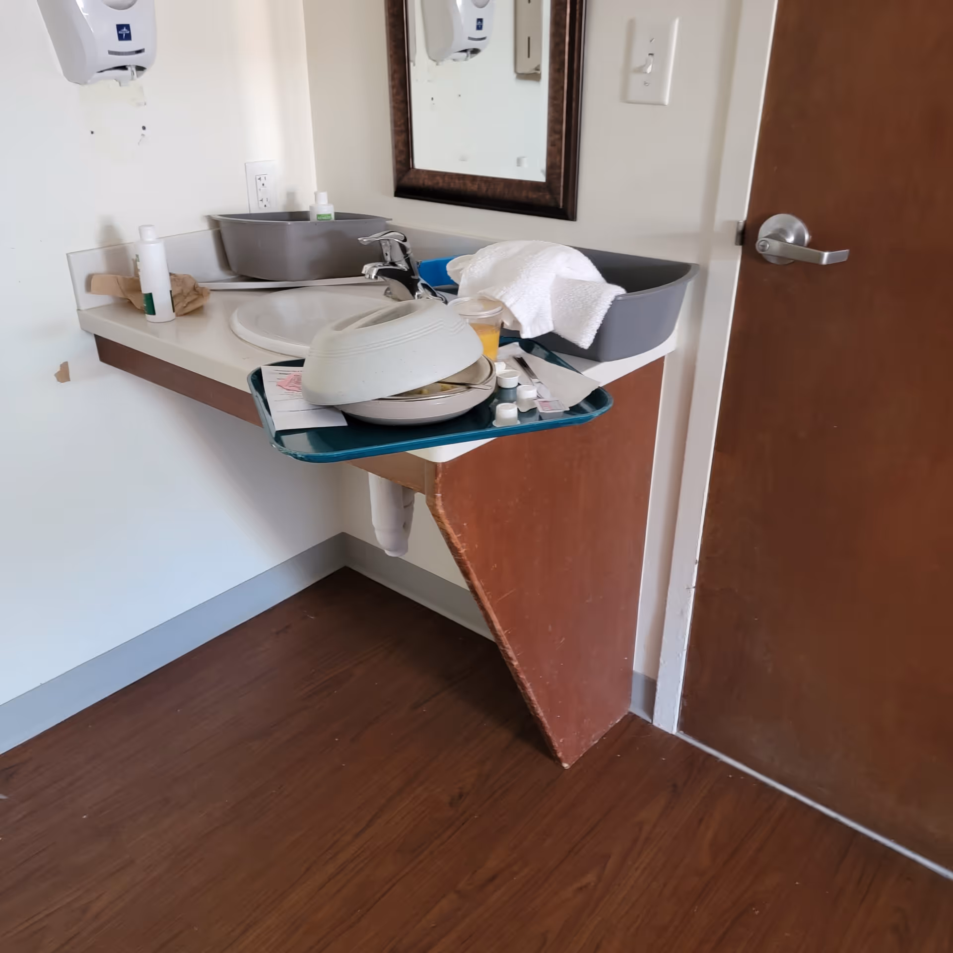 Messy bathroom sink area with dishes and a tray in a senior facility