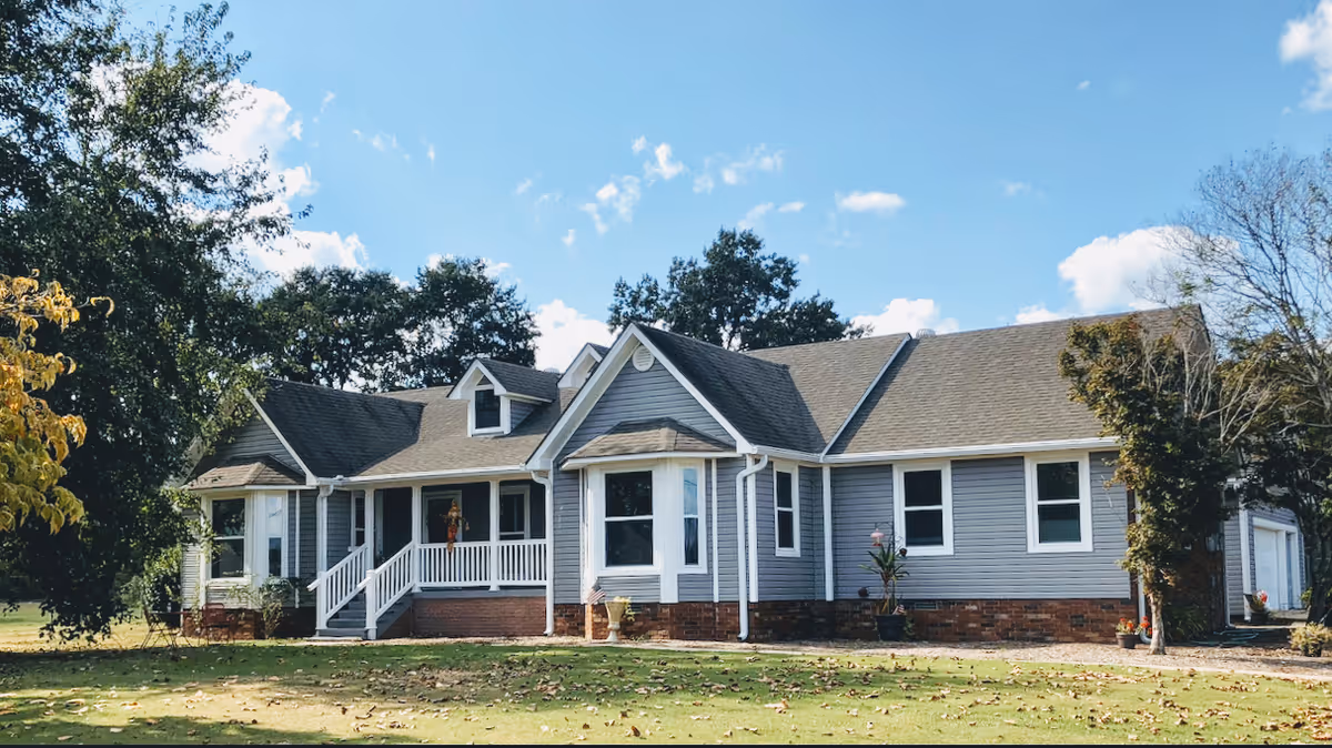 Grey, single-story care home exterior with a front porch and brick foundation.