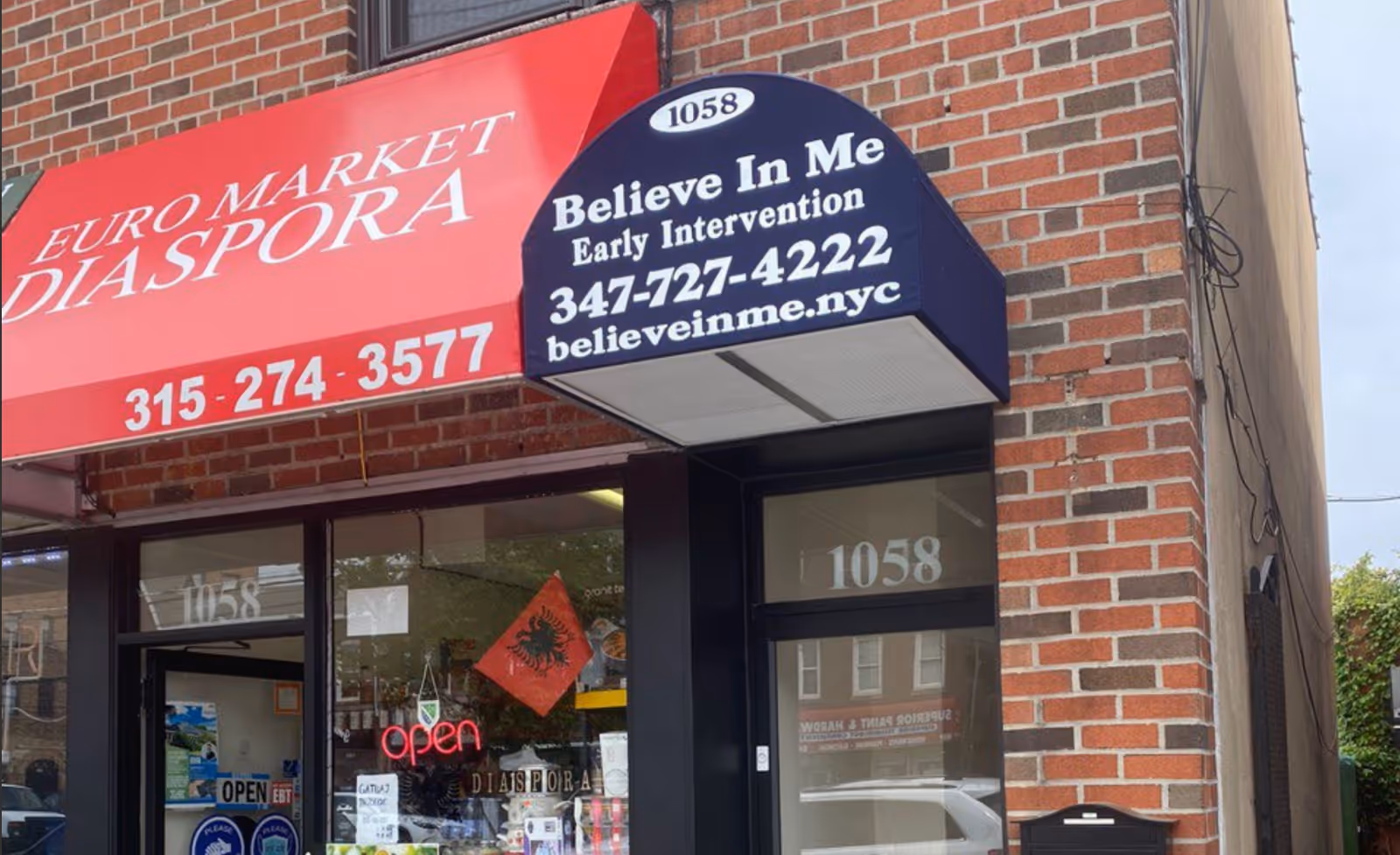Brick storefront with red awning and blue sign promoting Believe In Me Early Intervention.