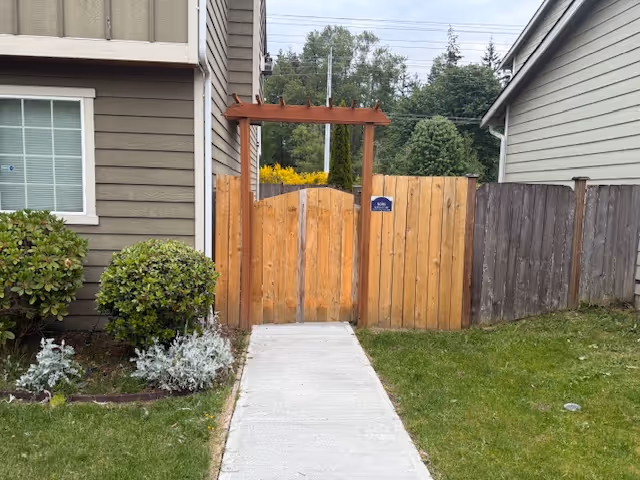Concrete walkway leads to a wooden gate between brown fences in a residential yard.