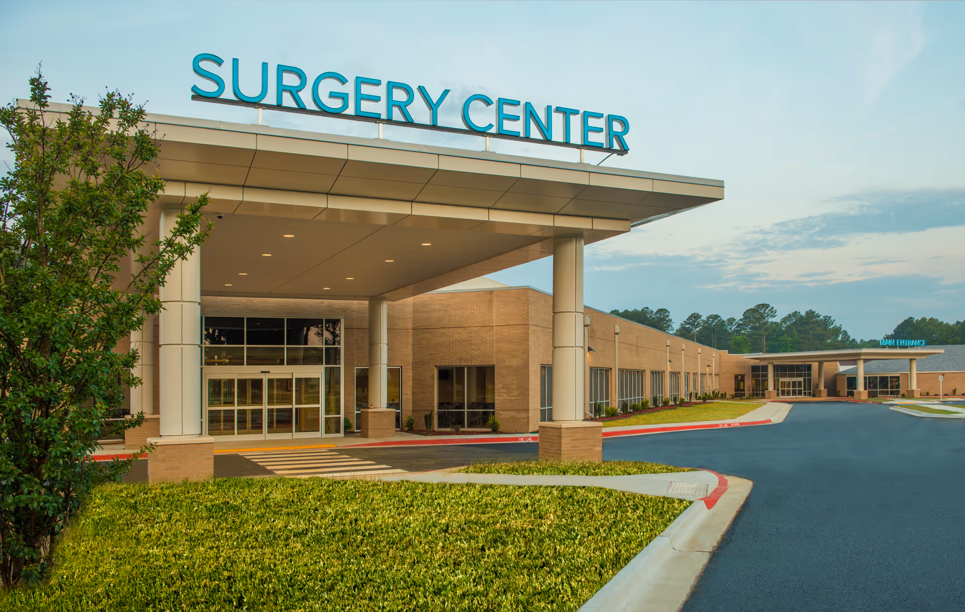 Exterior view of a medical facility with a large sign reading Surgery Center, entrance, and parking.