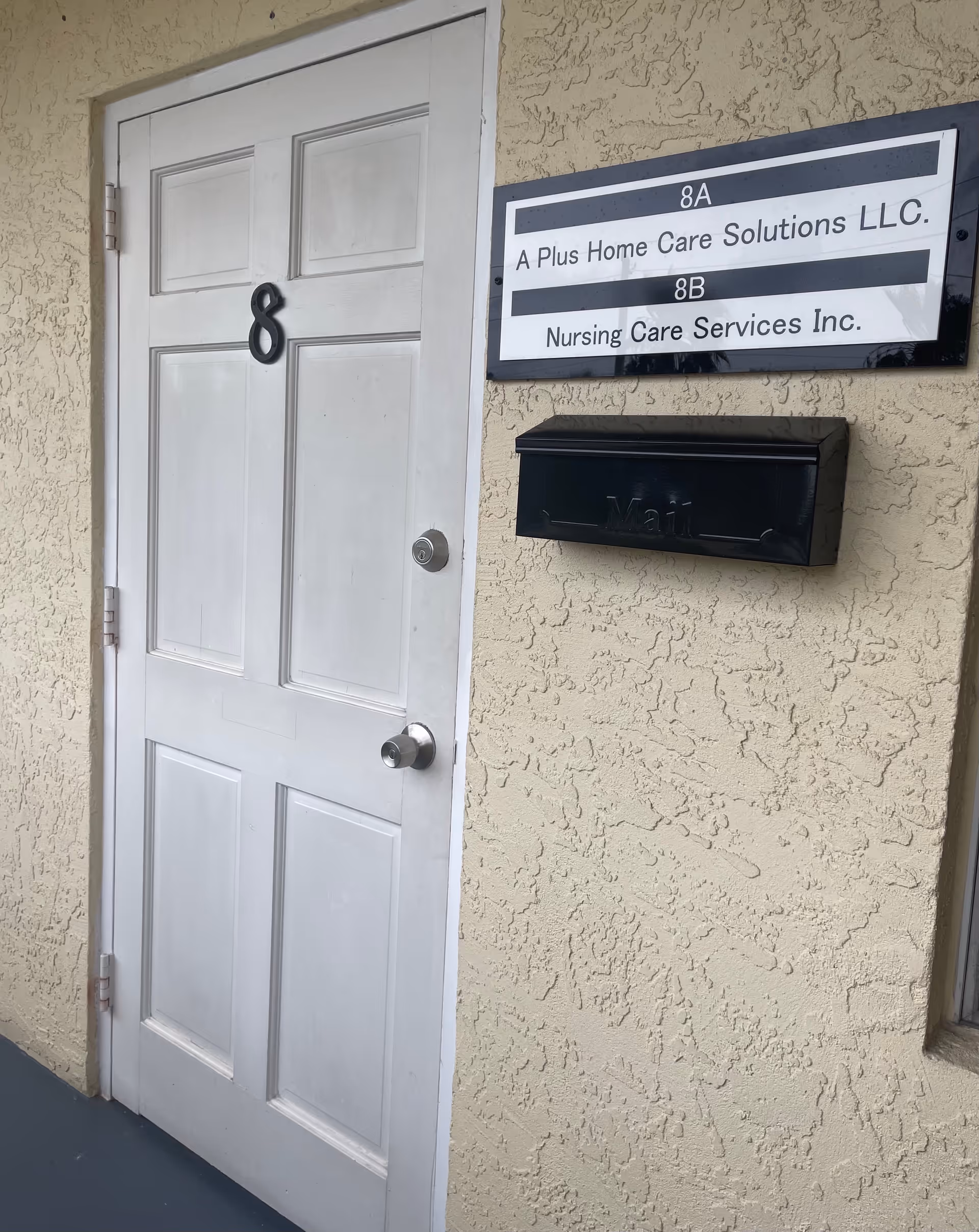 Exterior doorway with a sign reading 'A Plus Home Care Solutions LLC' and a black mailbox.