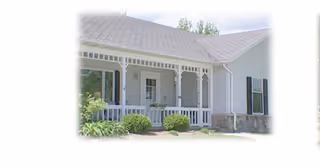 White single-story senior living facility with a covered porch and manicured shrubs.