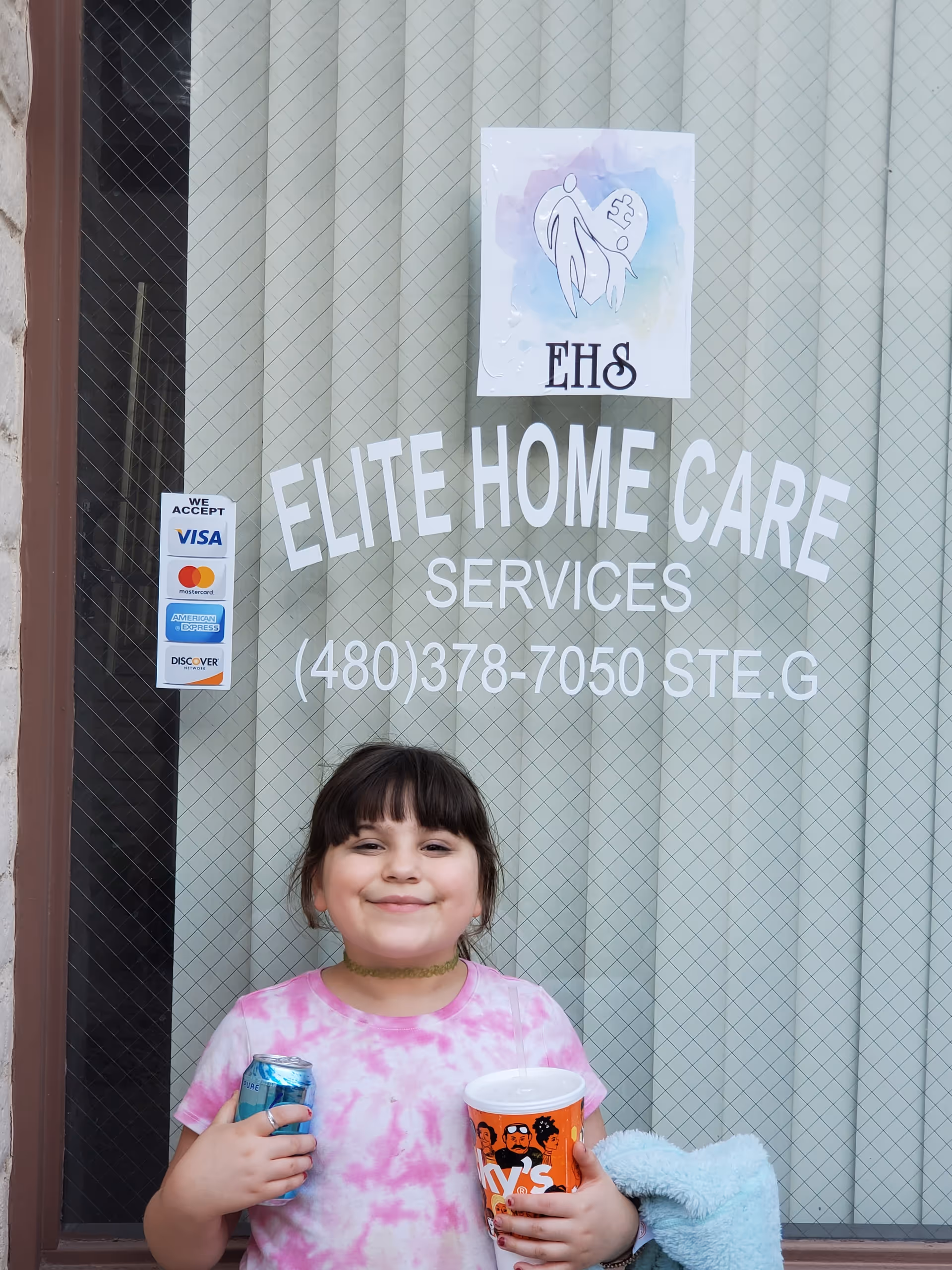 Smiling child stands outside Elite Home Care Services storefront window.