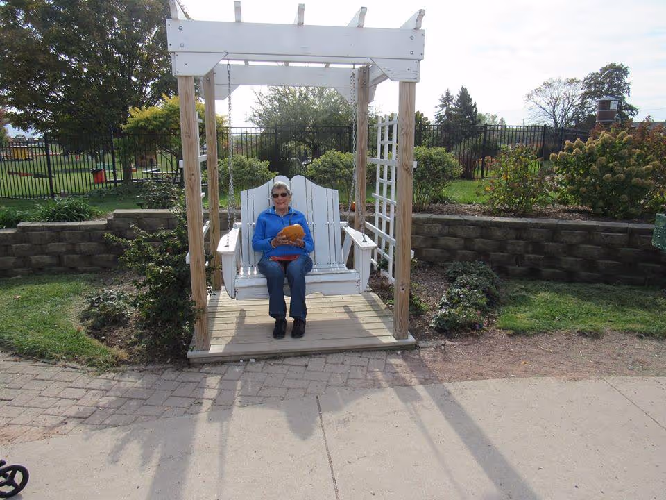 A woman sitting on a swing in a landscaped outdoor area at a senior living facility.