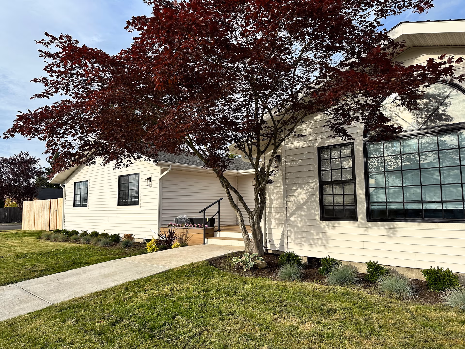 White single-story care home with large windows, a tree, and a sidewalk along the front.