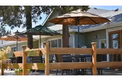 Outdoor patio with tables, umbrellas, and a wooden railing beside a building.