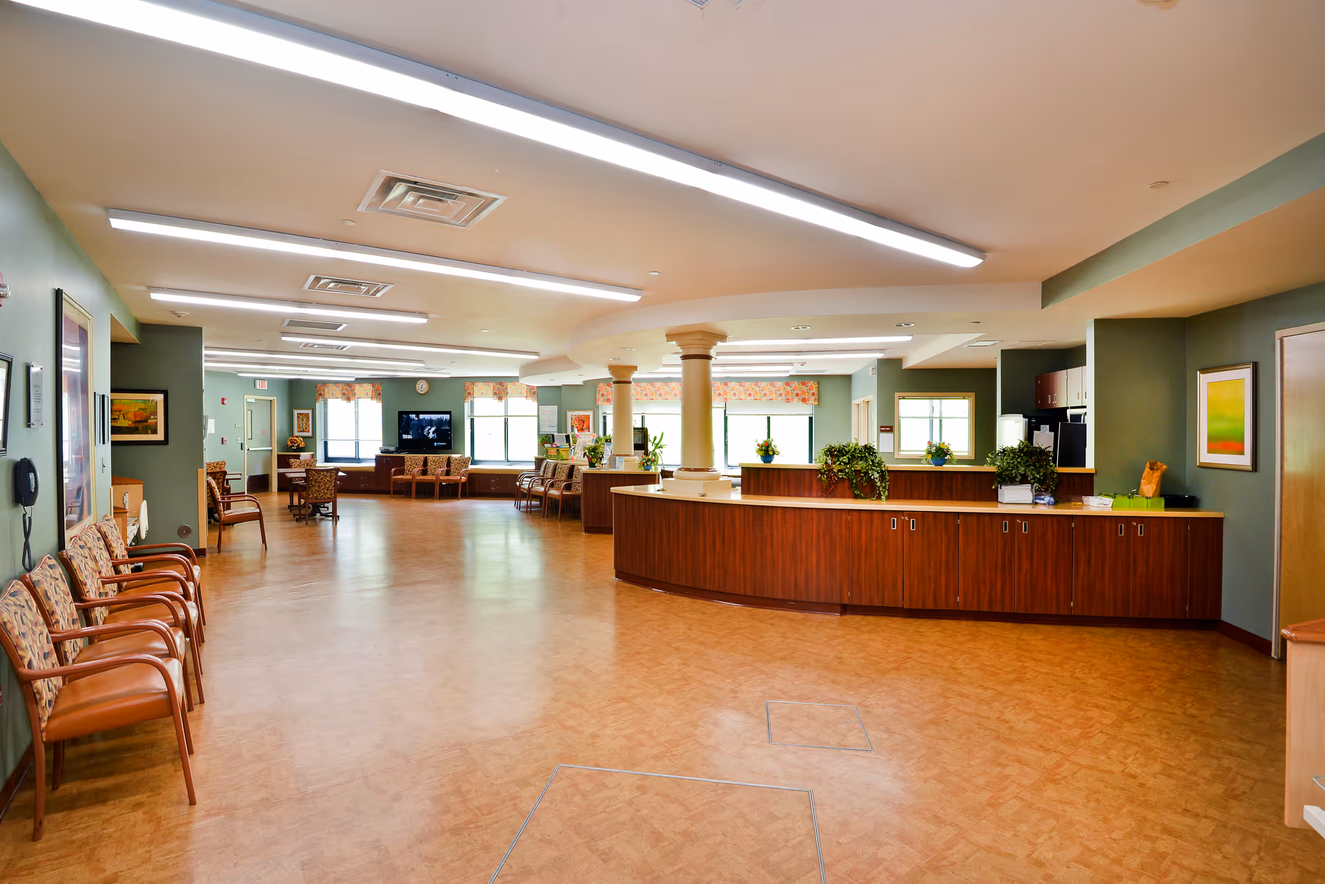 Spacious facility lobby with curved reception desk, seating, plants, and soft overhead lighting.
