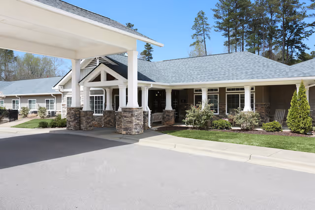 Front entrance of an assisted living building with a covered drop-off canopy, stone columns, and landscaped lawn.