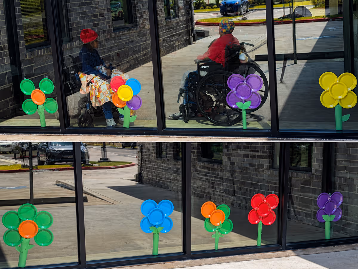 Glass-front exterior of Proverbial Care with colorful flower decals and residents in wheelchairs.