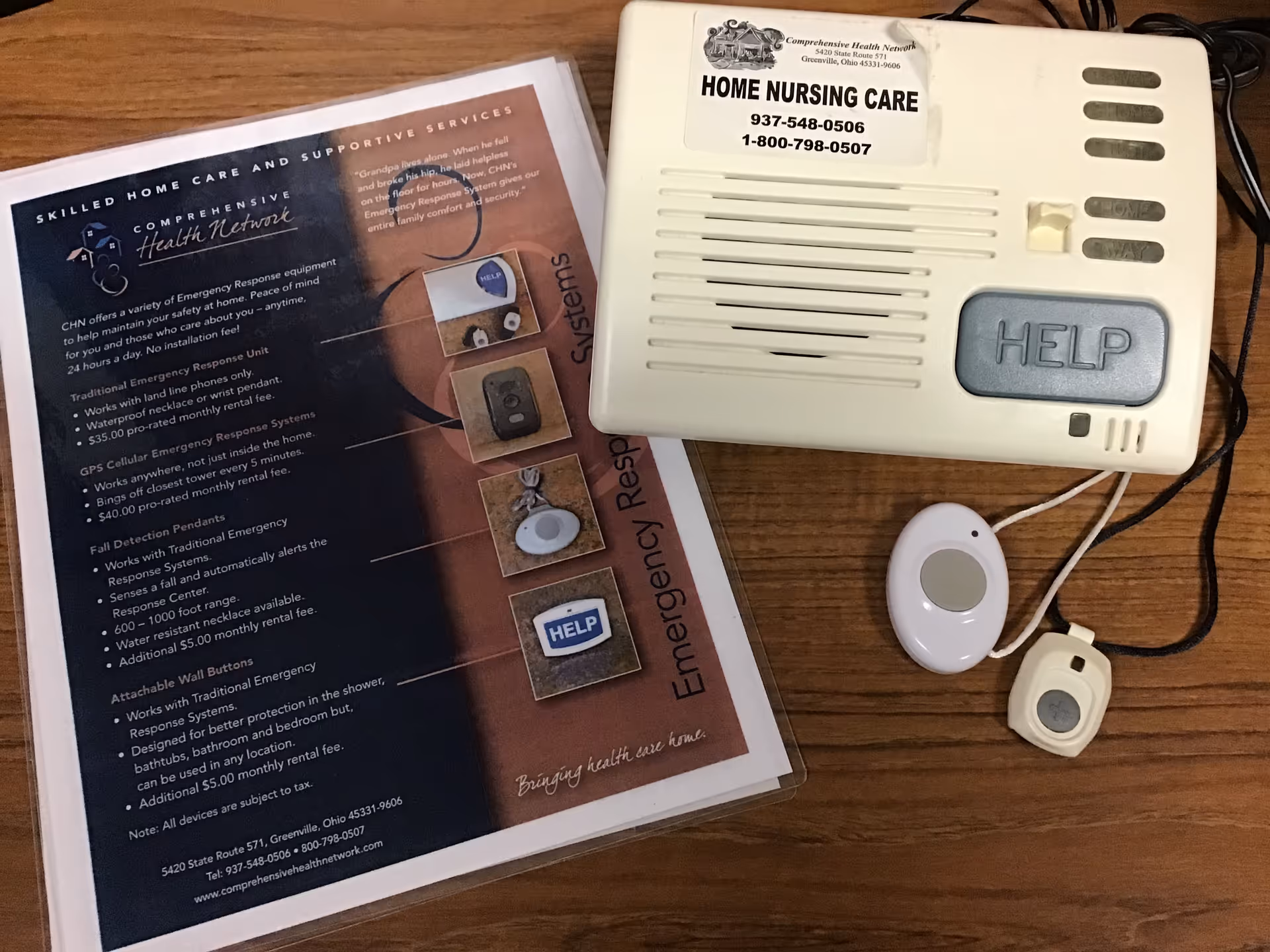 Close-up of a home nursing care emergency alert device and brochure on a wooden table.
