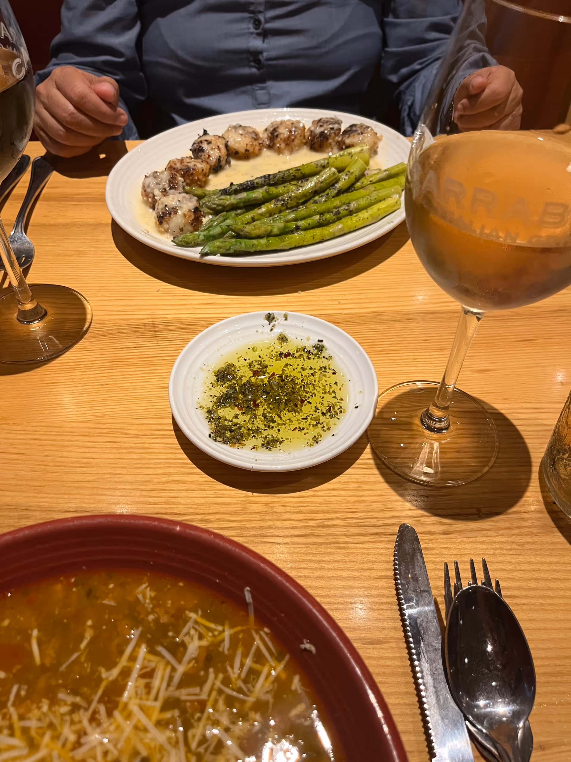 Dining table meal with asparagus, skewers, sauce, and drinks; hands visible.
