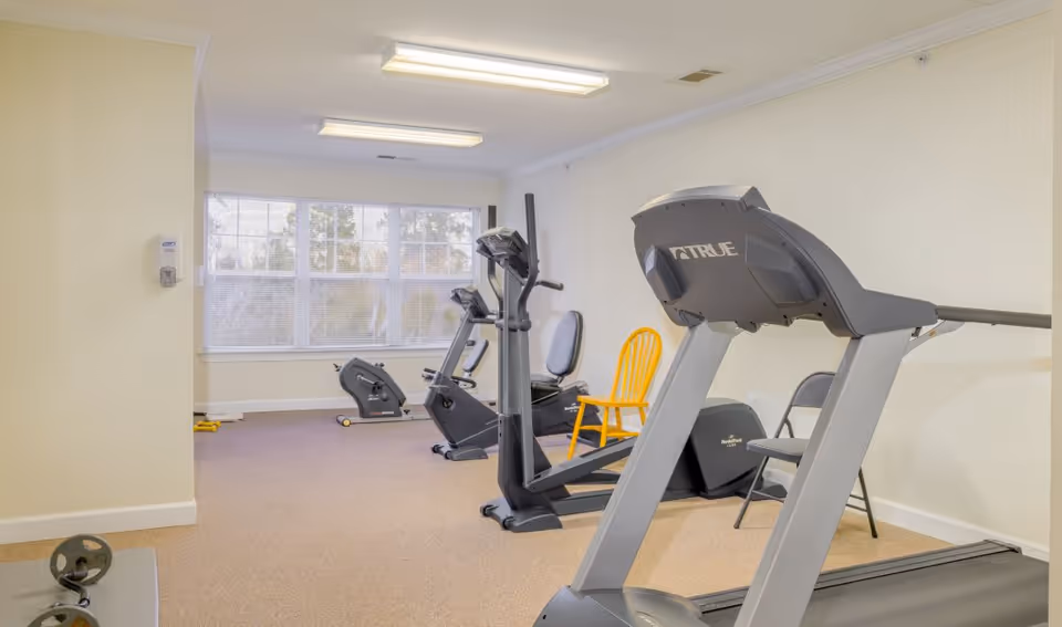 Interior fitness room with treadmills, a stationary bike, weights, and a yellow chair.
