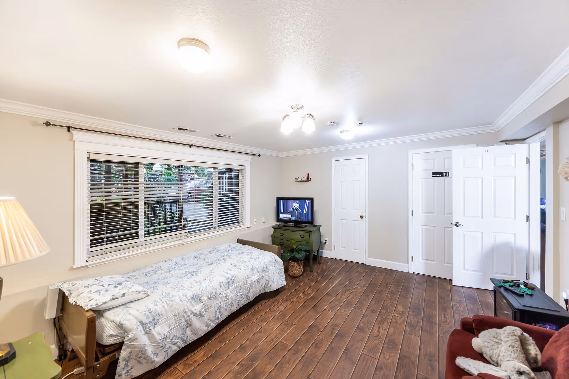 Senior living bedroom with a daybed, window blinds, and a TV on a small stand.