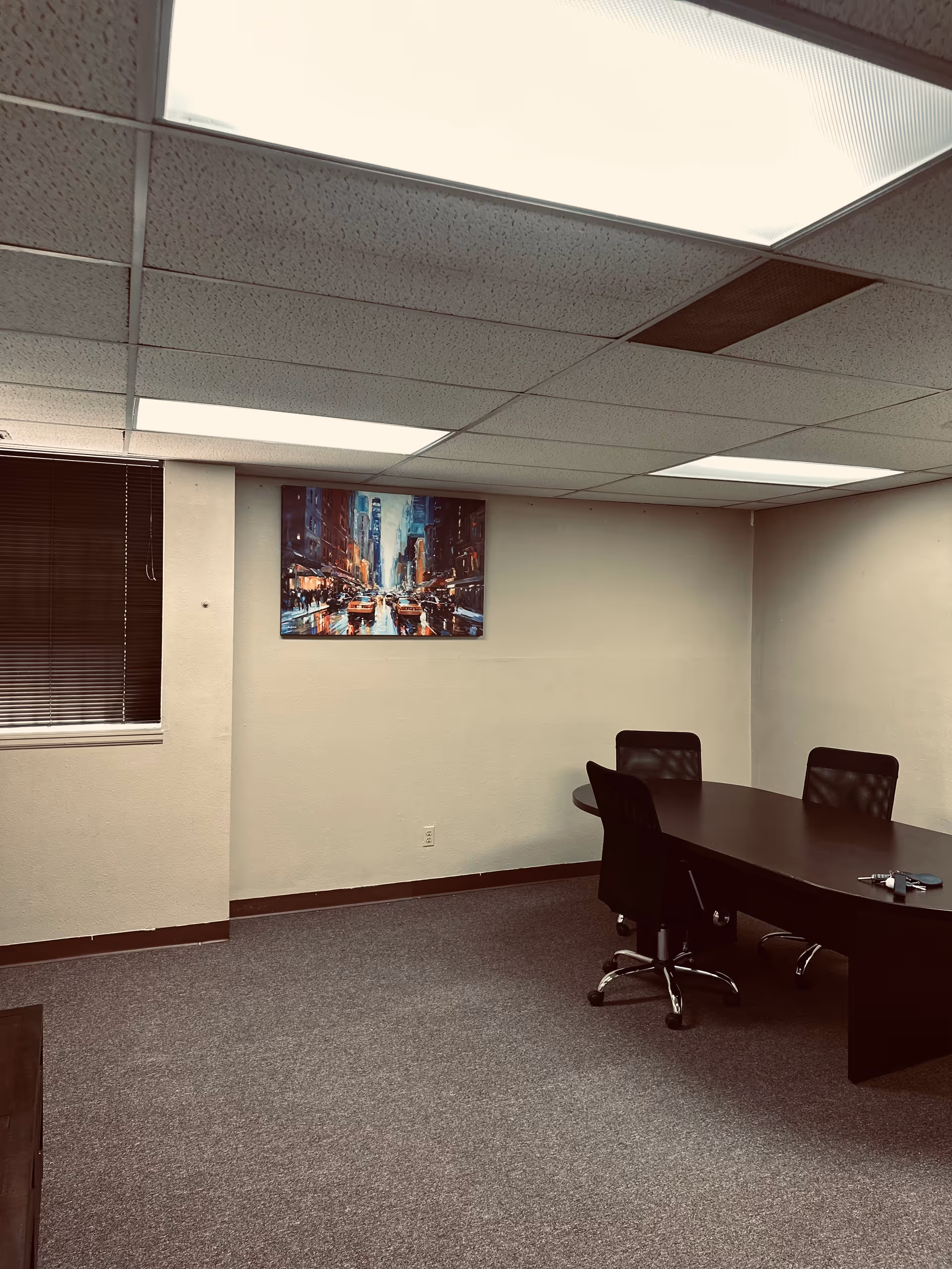Interior conference room with a dark table, black chairs, window blinds, and wall art.