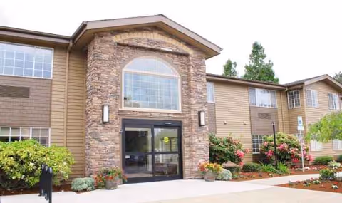 Exterior view of Emerald Gardens entrance with stone facade, glass doors, and landscaped surroundings.