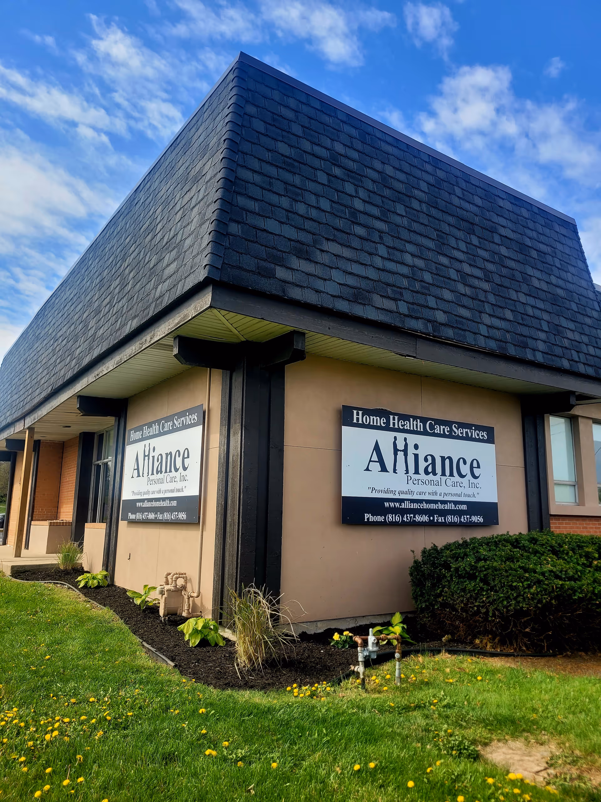 Exterior view of a beige senior care facility with Alliance Personal Care signage and blue sky.
