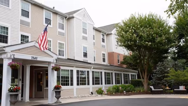 Exterior view of a multi-story senior living building with entrance and flag.