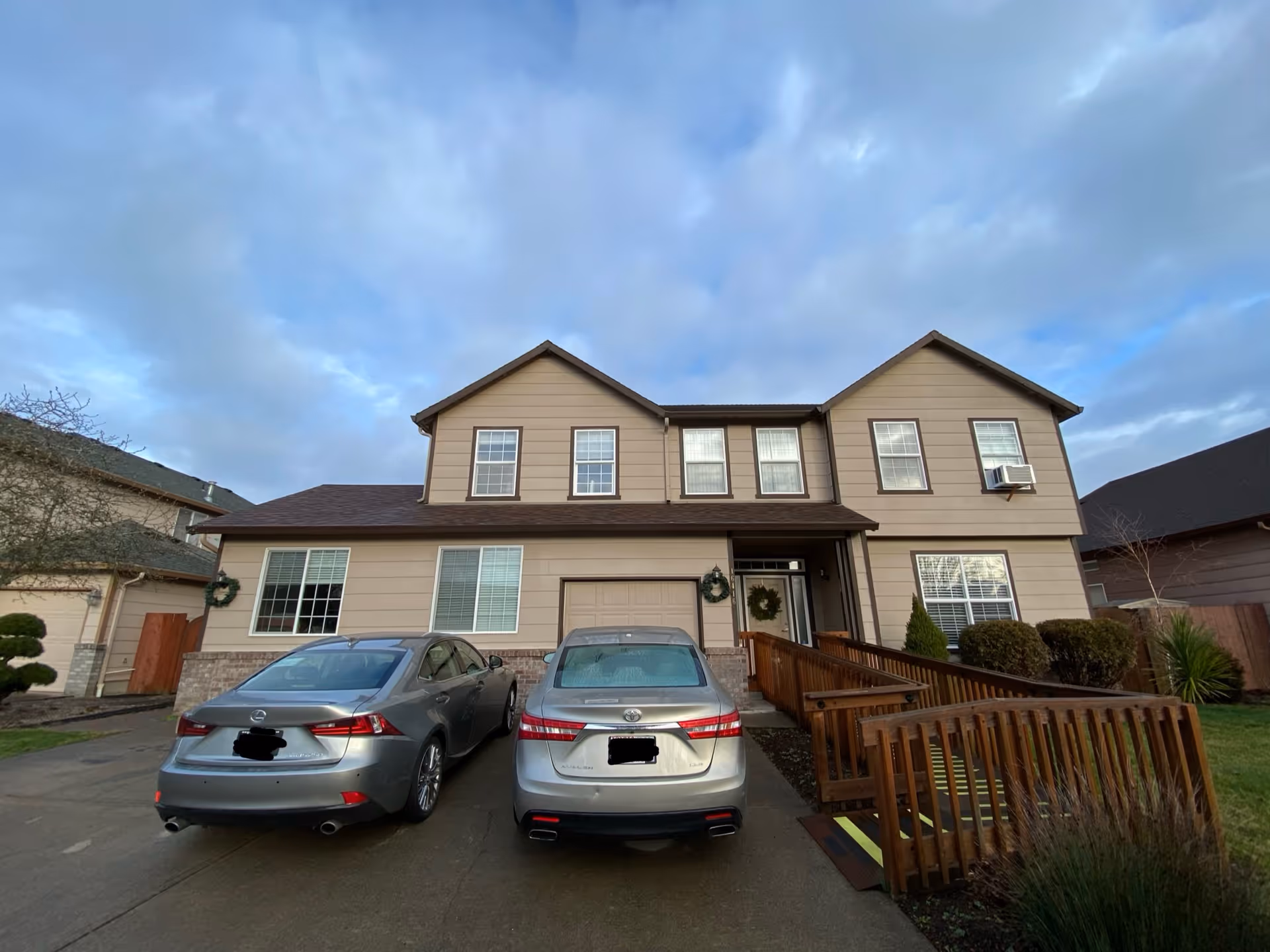 Front exterior of a two-story beige building with a wooden ramp, wreaths, and two parked cars.
