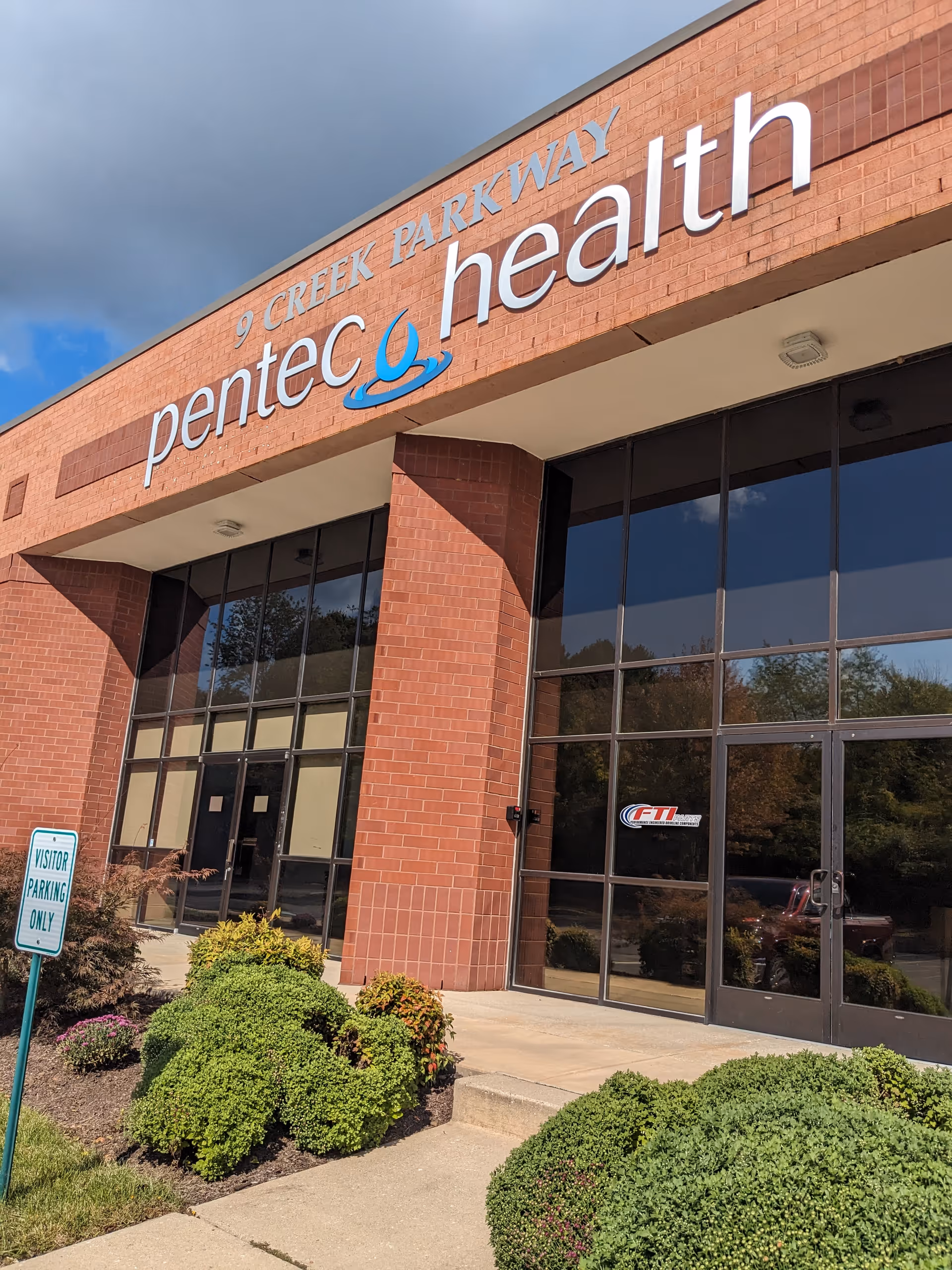 Exterior entrance of Pentec Health building showing brick facade, large glass doors, and trimmed shrubs.