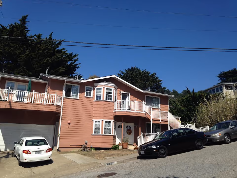 Pink two-story senior living building with balconies and parked cars.