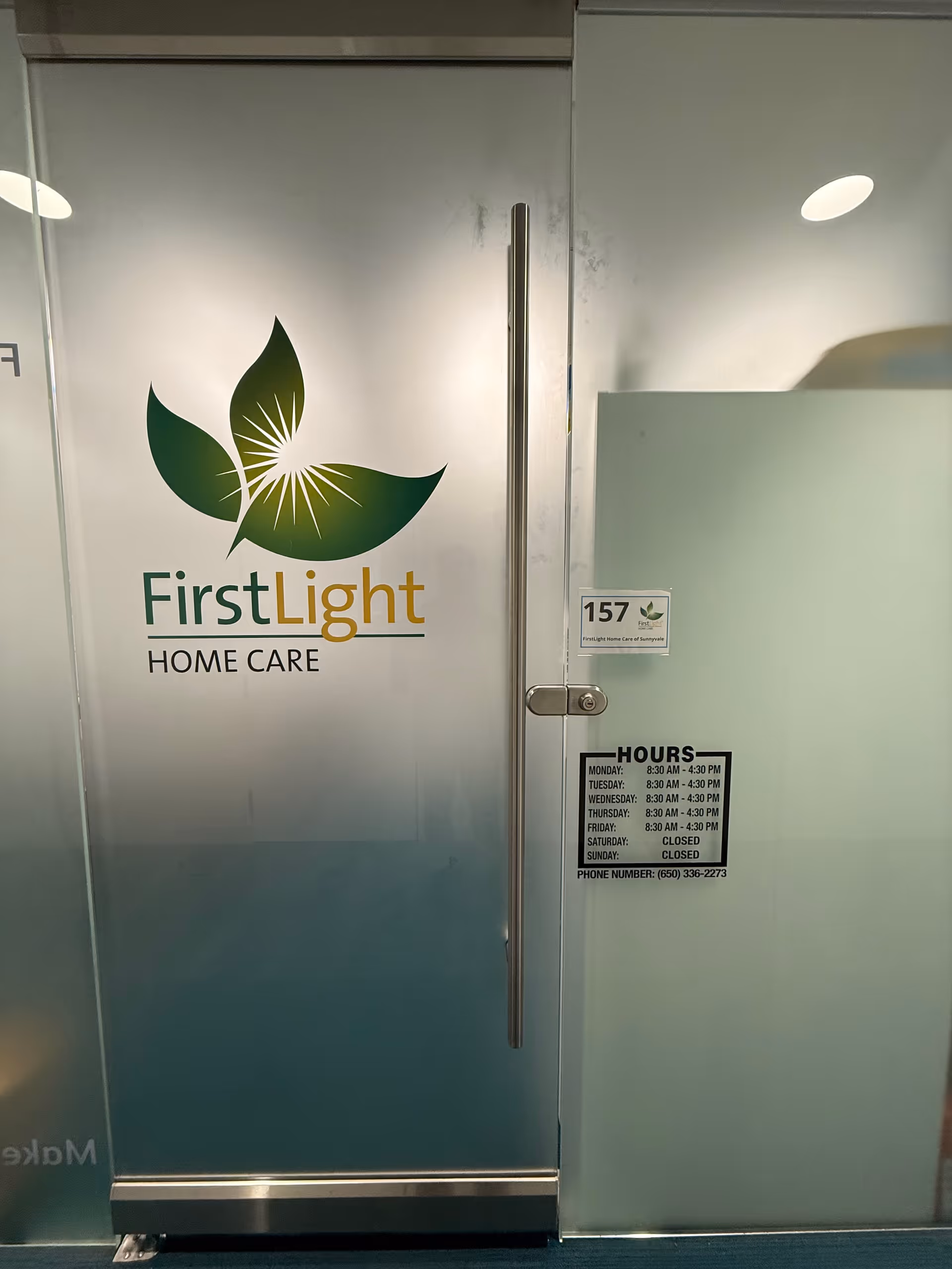 Glass door with FirstLight Home Care logo and hours sign in an interior hallway.