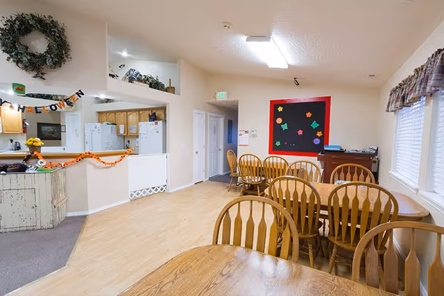 Communal dining area with multiple wooden tables and chairs, a kitchen pass-through, and seasonal decorations on the walls.