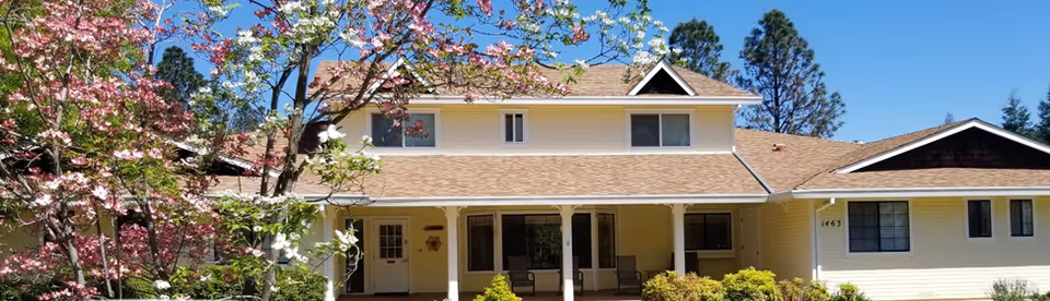 Sunshine assisted living cottage exterior with a covered porch and blooming trees.