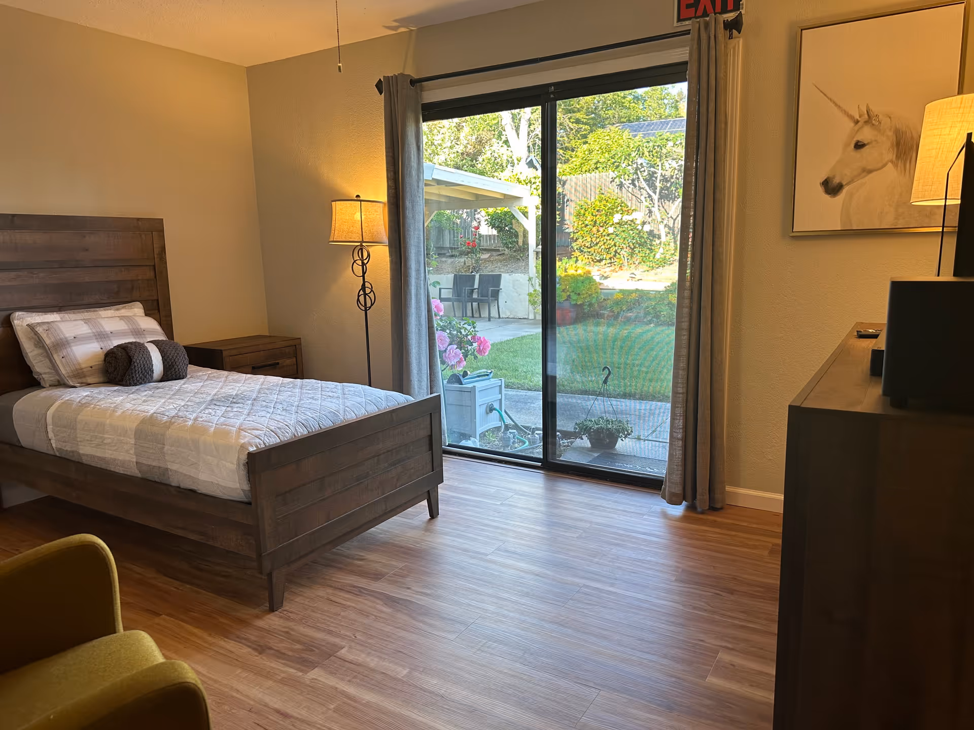 A furnished bedroom with a wooden bed, dresser, lamp, and sliding glass door to patio.