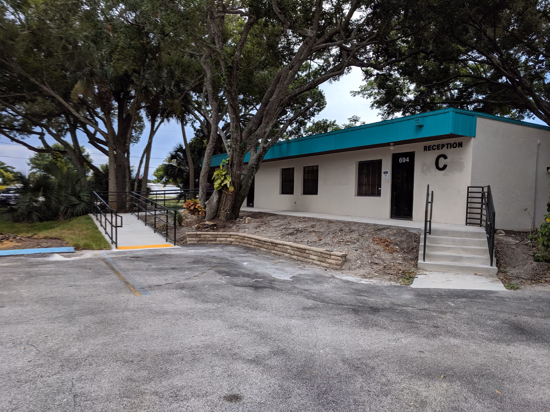 Exterior view of a facility entrance with ramp, stairs, and surrounding trees.