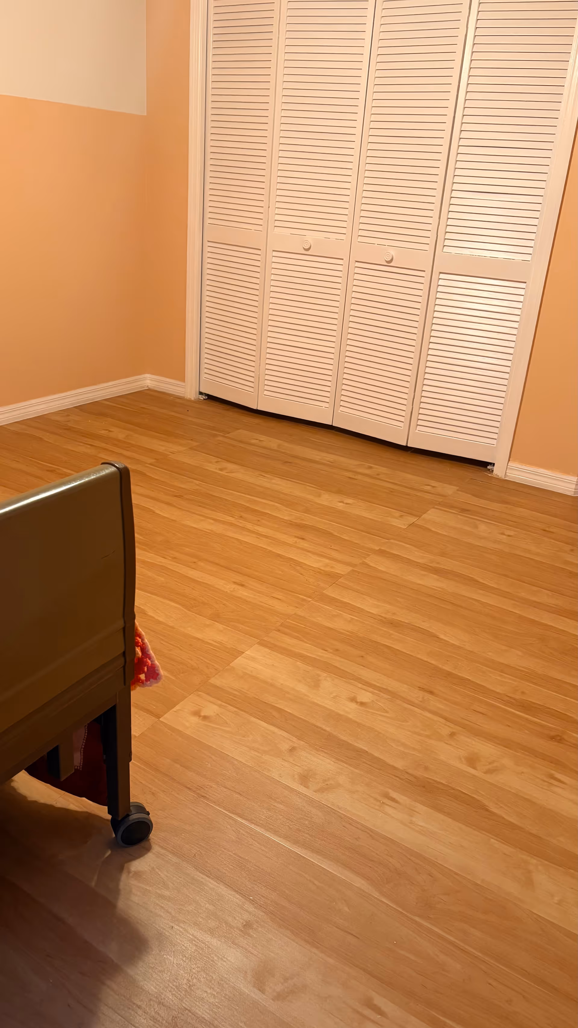 Bedroom corner with a bed, warm walls, wood floor, and white closet doors.