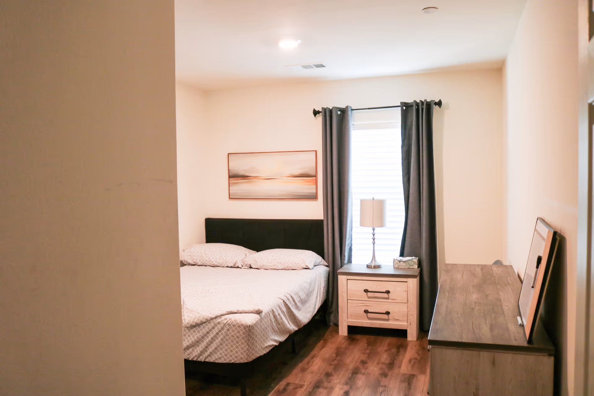 Cozy bedroom with a bed, nightstand, dresser, and curtains in soft neutral tones.