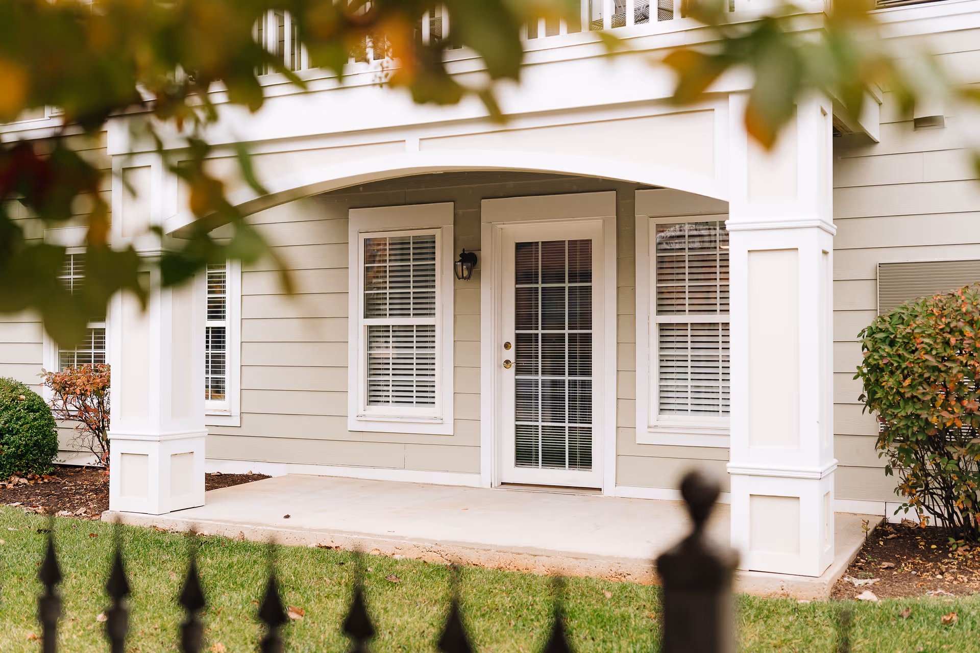 Covered ground-floor porch with a glass-paned door flanked by two windows and white columns on the front of a residential building.