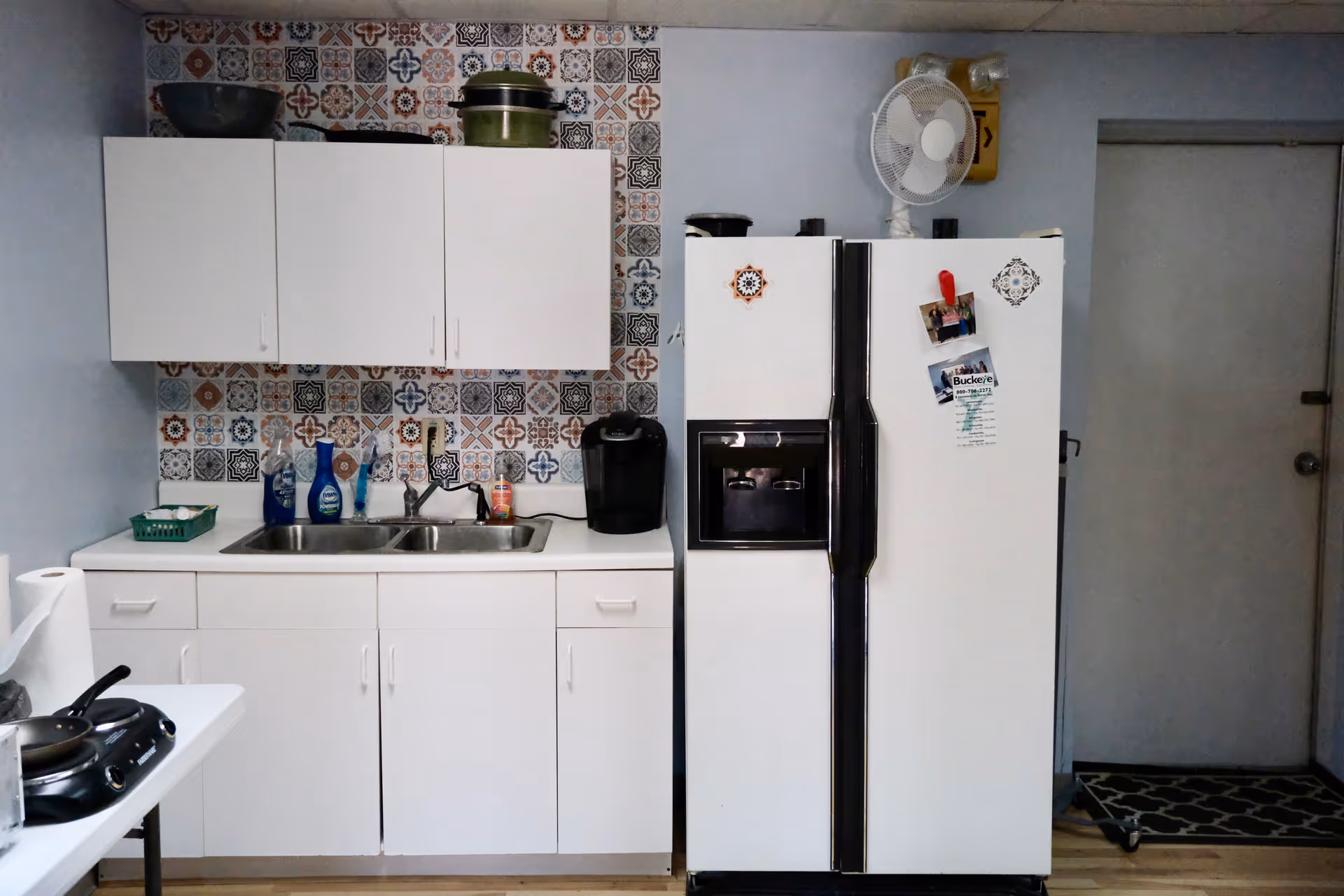 White kitchen with cabinets, sink, refrigerator, and patterned tile backsplash in a senior facility.