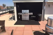 Outdoor rooftop patio with a built-in grill under a shaded alcove, surrounded by seating.