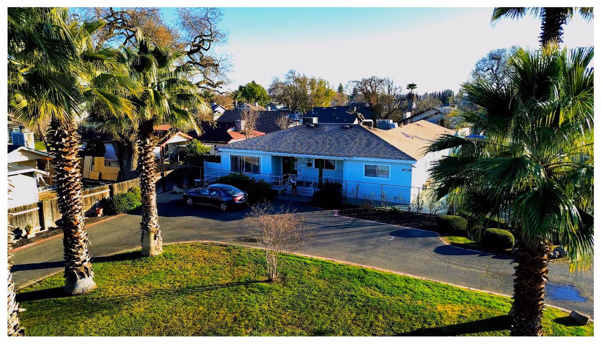 Exterior view of Lakewood Villa, a single-story blue building with palm trees and a parked car.