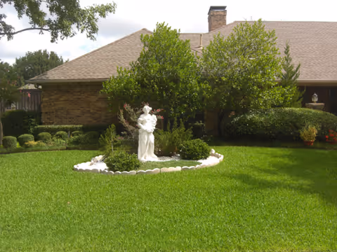 Statue in a circular flower bed on manicured lawn in front of brick facility.