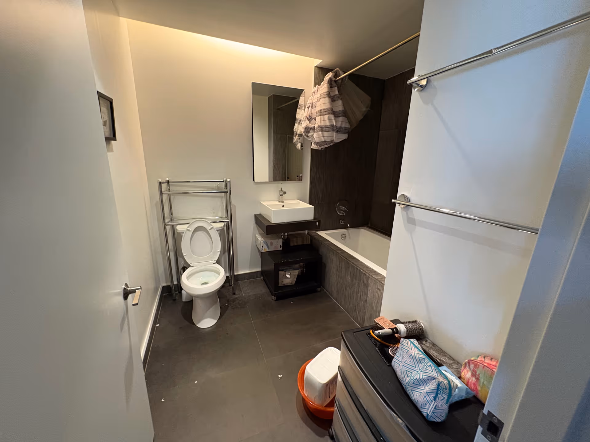 Modern bathroom featuring toilet, sink, bathtub, mirror, towels, and shelving.