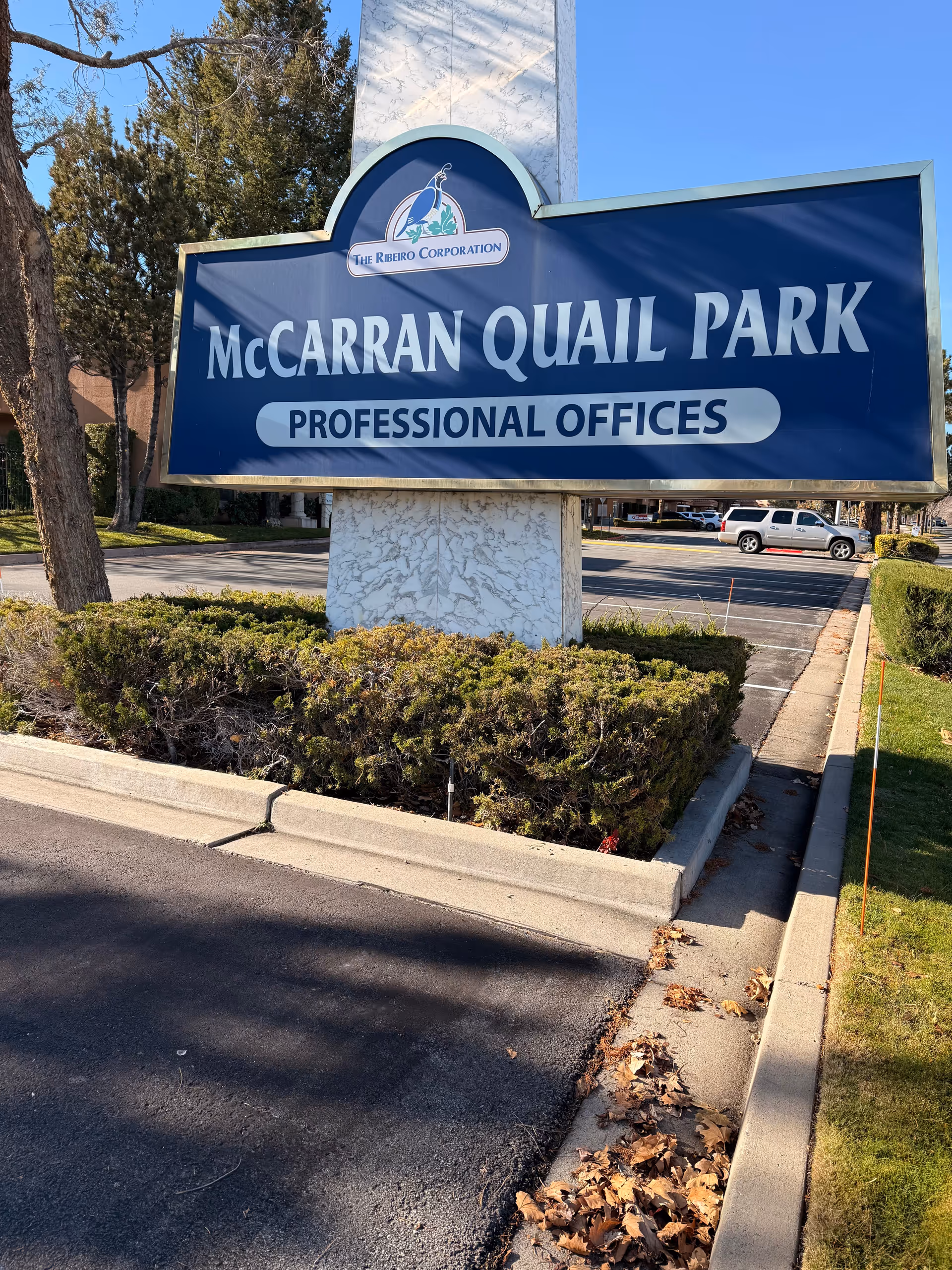 A large blue sign for McCarran Quail Park Professional Offices beside a parking lot.