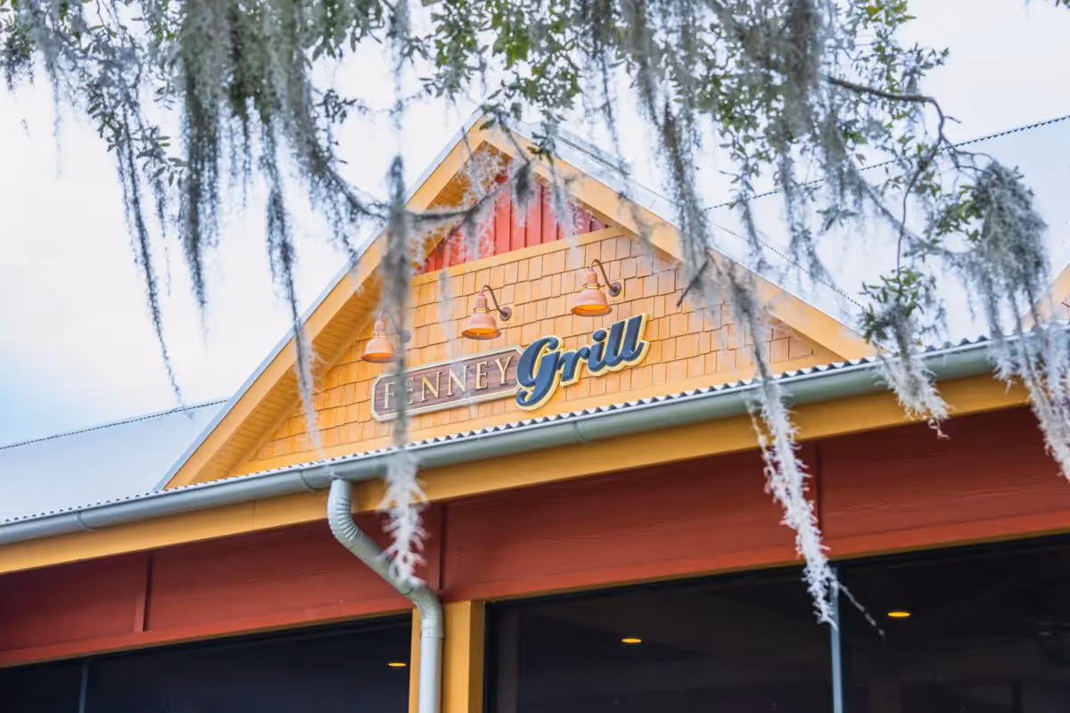 Exterior view of a building facade with a yellow gable and a Fenney Grill sign, framed by hanging branches.