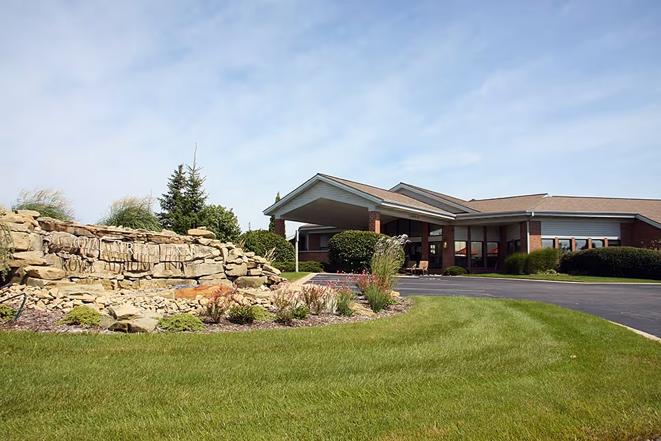Brick assisted-living building with a covered entrance and a stone sign reading 'Royal Atrium Inn' set in landscaped lawn.