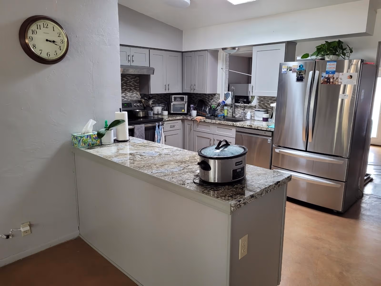 Grey kitchen with island, stainless appliances, sink, and clock on the wall.