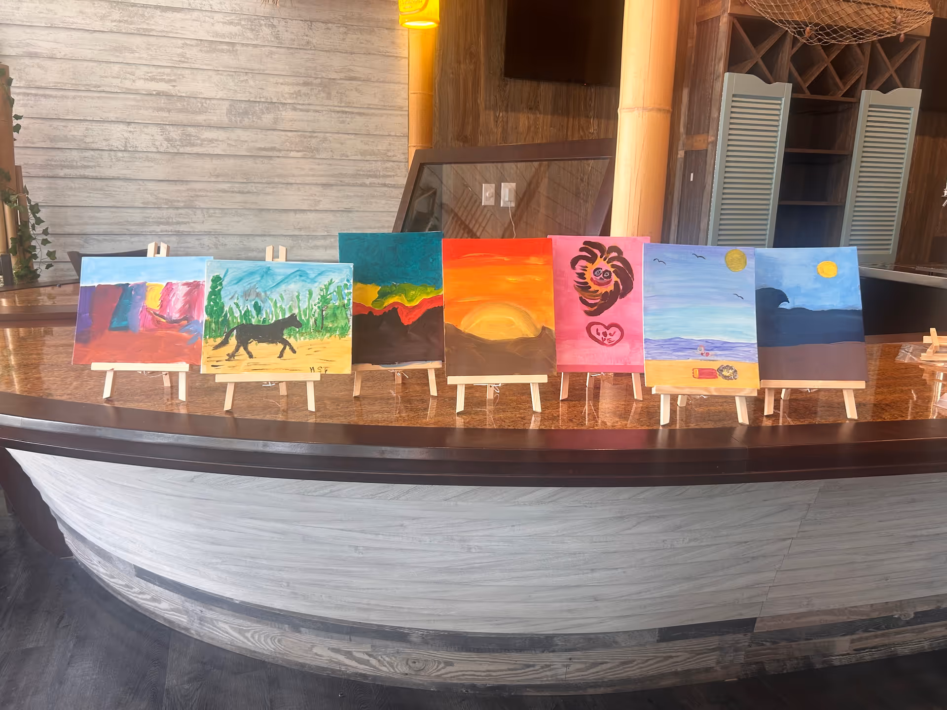 Row of colorful paintings on small easels lined along a curved marble counter.