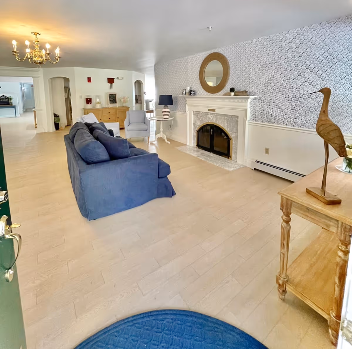 Spacious living room area with blue couch, fireplace, patterned wallpaper, and decorative bird statue.