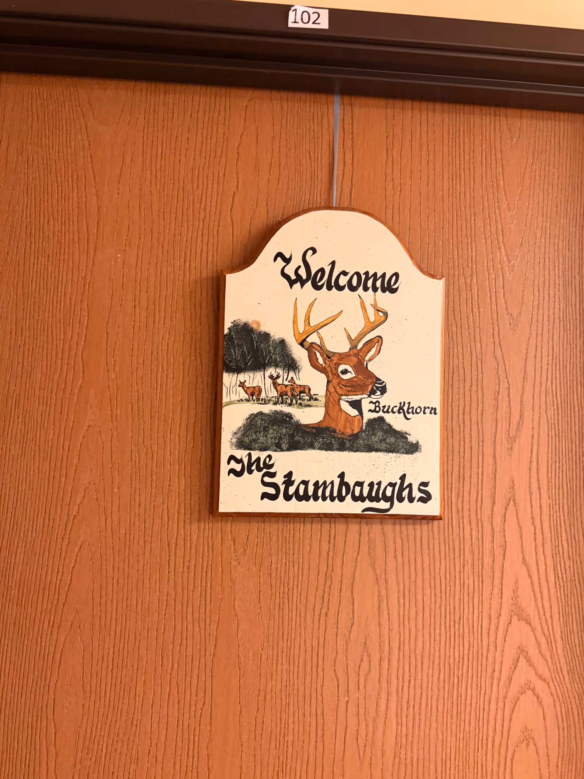 Wood-paneled wall with a decorative Welcome Buckhorn The Stambaughs sign.
